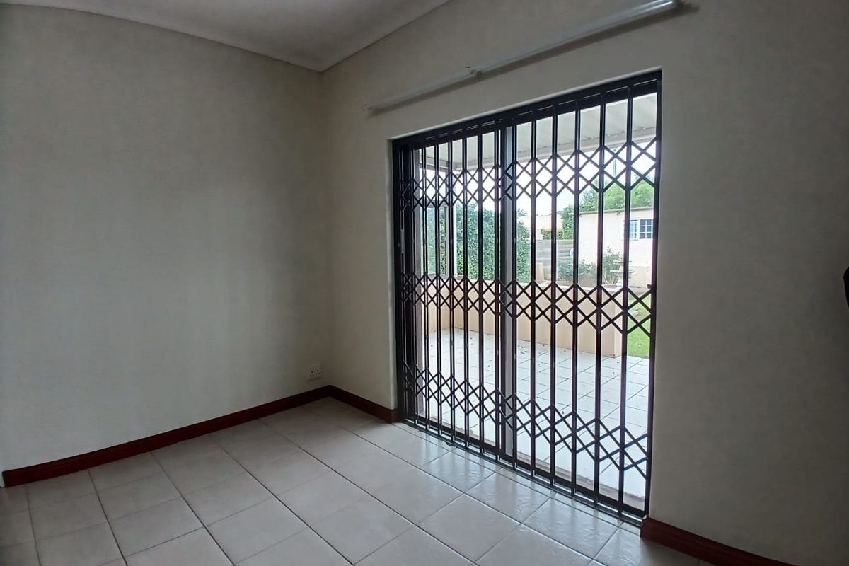 An empty living room featuring tiled flooring and a sliding glass door with a security gate, providing direct access to the outdoor patio area.