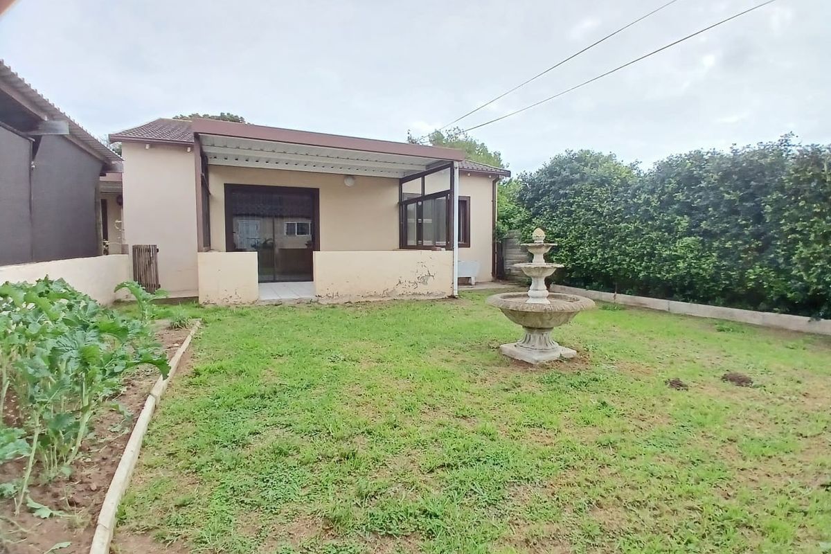Rear view of the cottage featuring a covered patio, sliding glass doors, and a private garden with a central fountain and established hedge boundary.