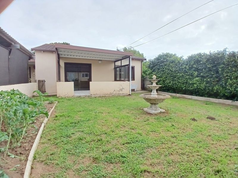 Rear view of the cottage featuring a covered patio, sliding glass doors, and a private garden with a central fountain and established hedge boundary.