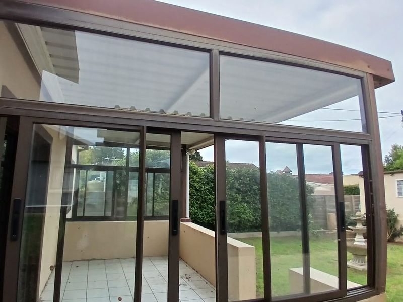 A covered patio area featuring sliding glass doors, tiled flooring, and aluminum frames, overlooking the rear garden space.