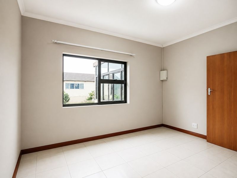 A clean, empty bedroom featuring neutral wall tones, tiled flooring, and a modern aluminium window frame, providing a versatile space ready for furnishing.
