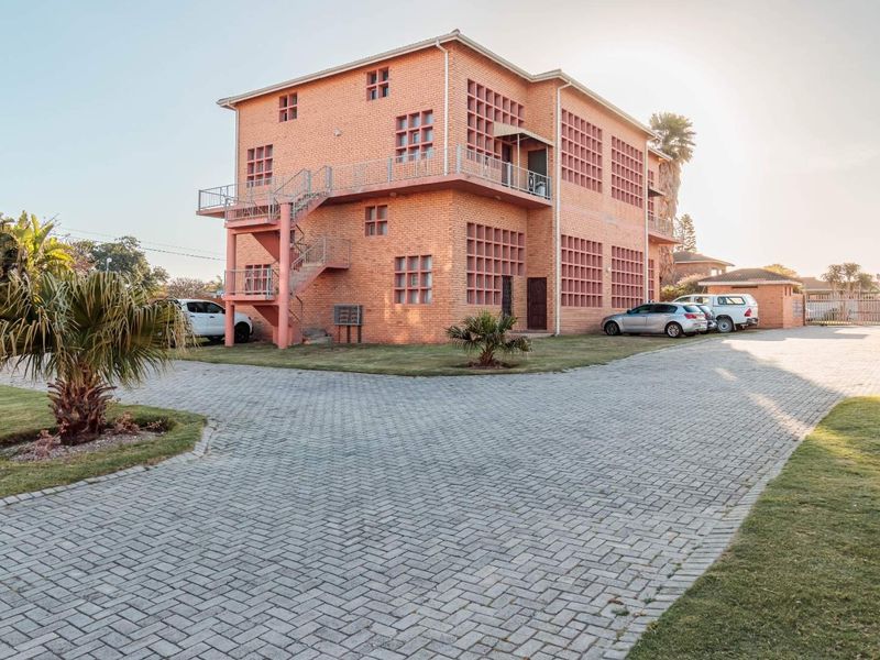 A multi-story brick apartment building featuring external staircases, lattice brick detailing, and a paved driveway with ample parking space.