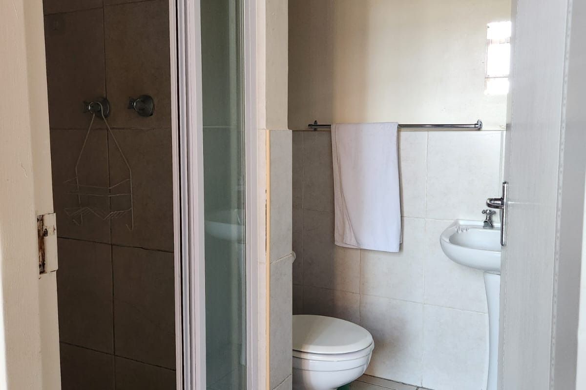 A functional bathroom featuring a shower enclosure, pedestal basin, toilet, tiled finishes, and exposed timber ceiling beams.