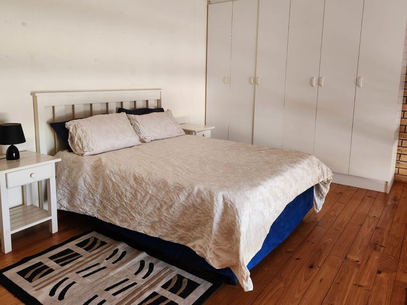 Spacious bedroom featuring warm timber flooring, extensive built-in cupboard storage, and a rustic exposed brick feature wall.