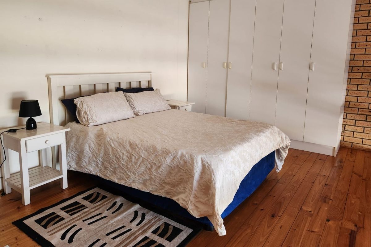Spacious bedroom featuring warm timber flooring, extensive built-in cupboard storage, and a rustic exposed brick feature wall.