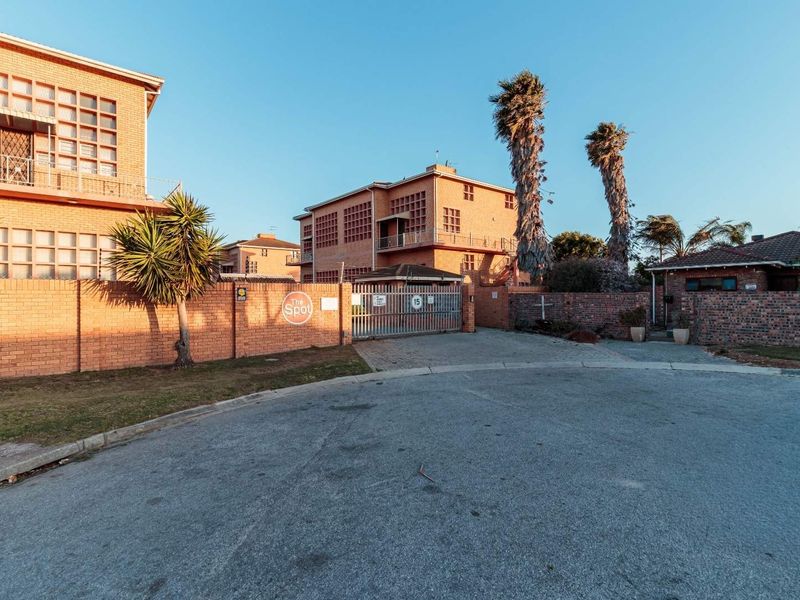 Front exterior view of a multi-story brick apartment complex featuring a secure gated entrance and paved driveway access.