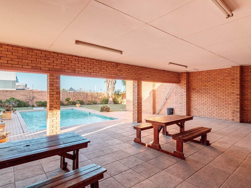 Spacious covered patio area featuring brick construction and tiled flooring, overlooking a private swimming pool and garden.