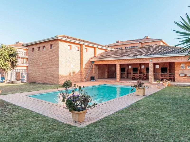 Communal outdoor area featuring a swimming pool, brick-paved surround, and a covered patio with built-in braai facilities.