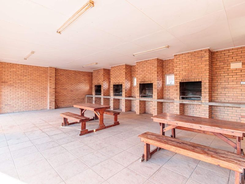 Covered outdoor entertainment area featuring multiple built-in brick braais, concrete prep counters, and durable tiled flooring.