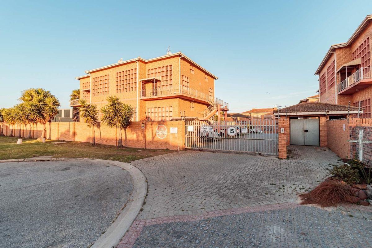 Front exterior view of a brick apartment complex featuring a secure gated entrance, paved driveway, and perimeter wall with electric fencing.