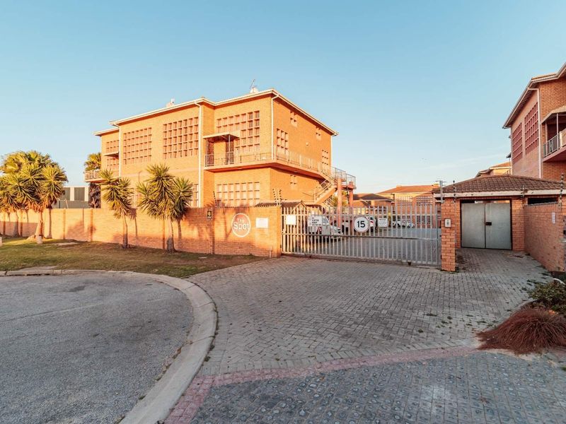 Front exterior view of a brick apartment complex featuring a secure gated entrance, paved driveway, and perimeter wall with electric fencing.