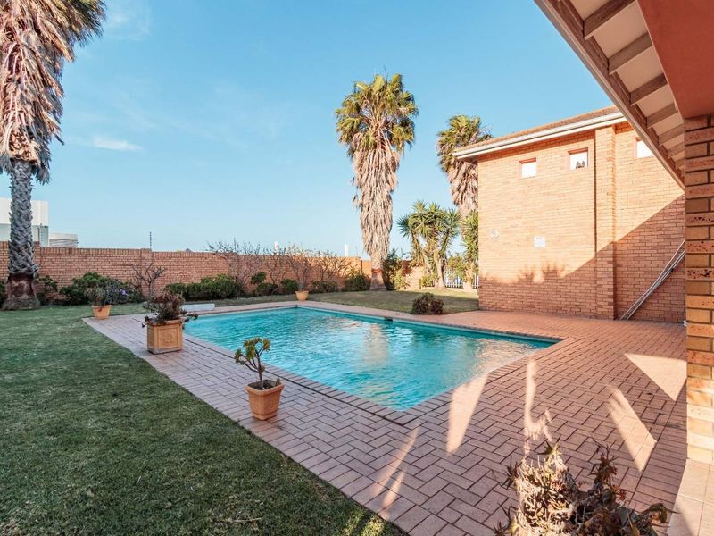 A private outdoor pool area featuring a paved surround, a brick boundary wall, and a covered patio space.