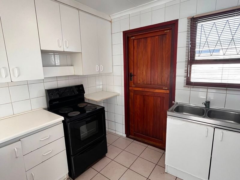 Functional kitchen featuring white cabinetry, tiled splashbacks, double basin sink, and tiled flooring, providing a practical workspace with direct external access.