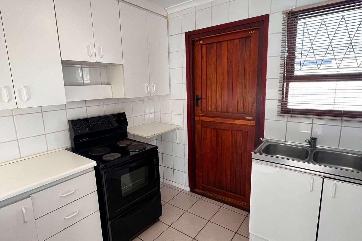 Functional kitchen featuring white cabinetry, tiled splashbacks, double basin sink, and tiled flooring, providing a practical workspace with direct external access.