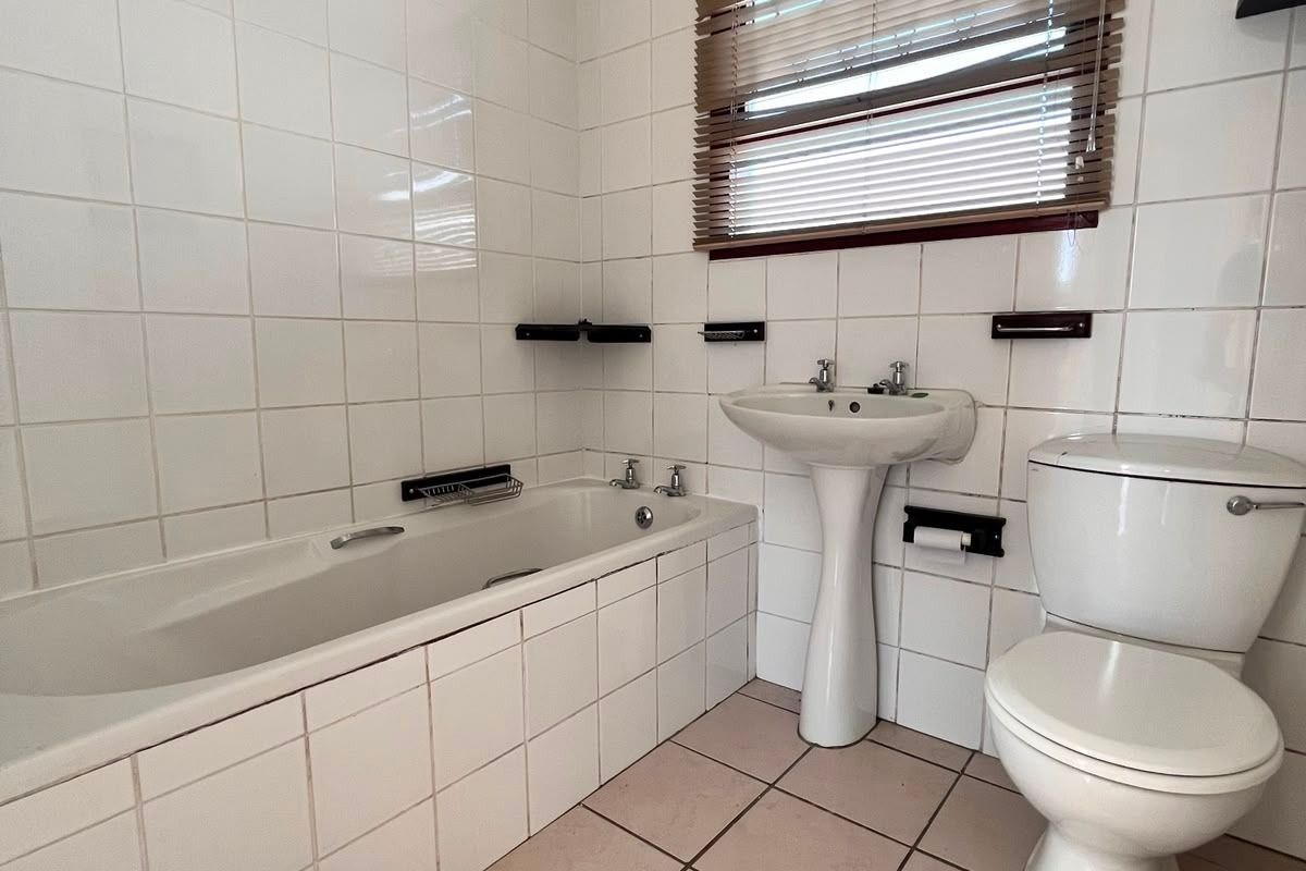 A functional bathroom featuring a pedestal basin, built-in bathtub, and toilet with neutral wall and floor tiling.