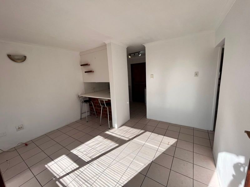 An open-plan living area featuring neutral ceramic floor tiles and a built-in breakfast counter with a brick base.