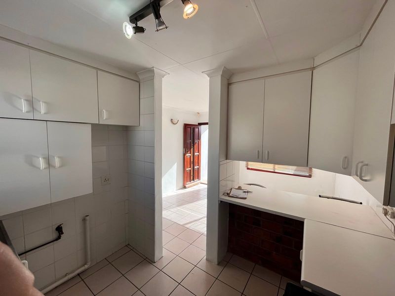 A functional scullery area featuring built-in white cabinetry, tiled flooring, and dedicated plumbing connections, providing a practical space for laundry or additional kitchen prep.