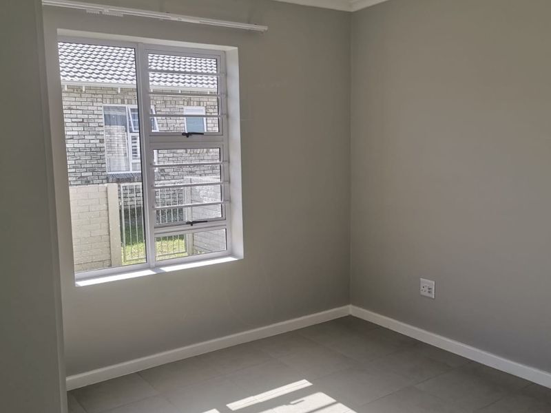 A clean, empty bedroom featuring neutral grey walls, tiled flooring, and an aluminium window with security bars.