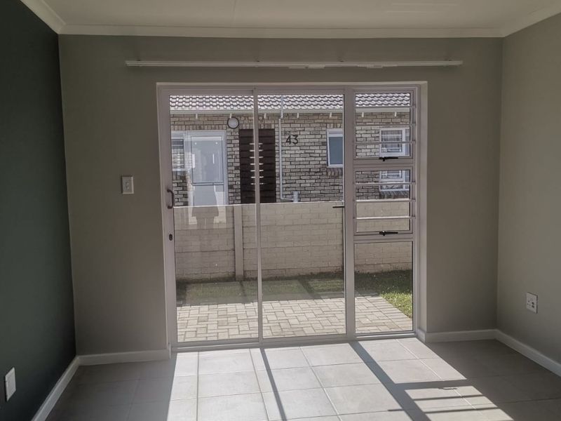 A bright, empty living room featuring neutral tiled flooring and a sliding glass door that opens onto a paved patio area.