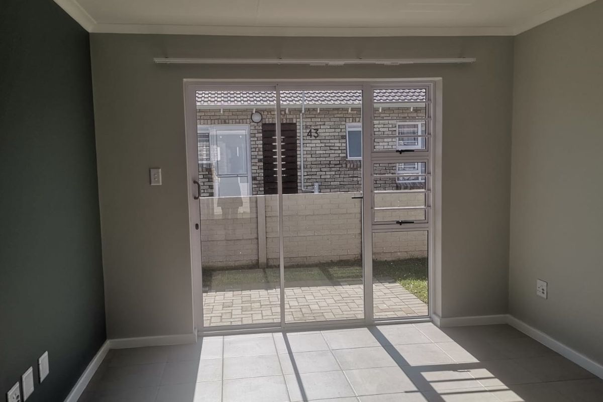 A bright, empty living room featuring neutral tiled flooring and a sliding glass door that opens onto a paved patio area.