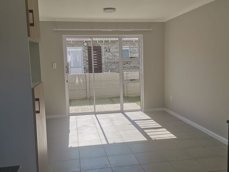 Bright open-plan living area featuring neutral tiled flooring, built-in cabinetry, and a sliding glass door providing direct access to the rear patio.