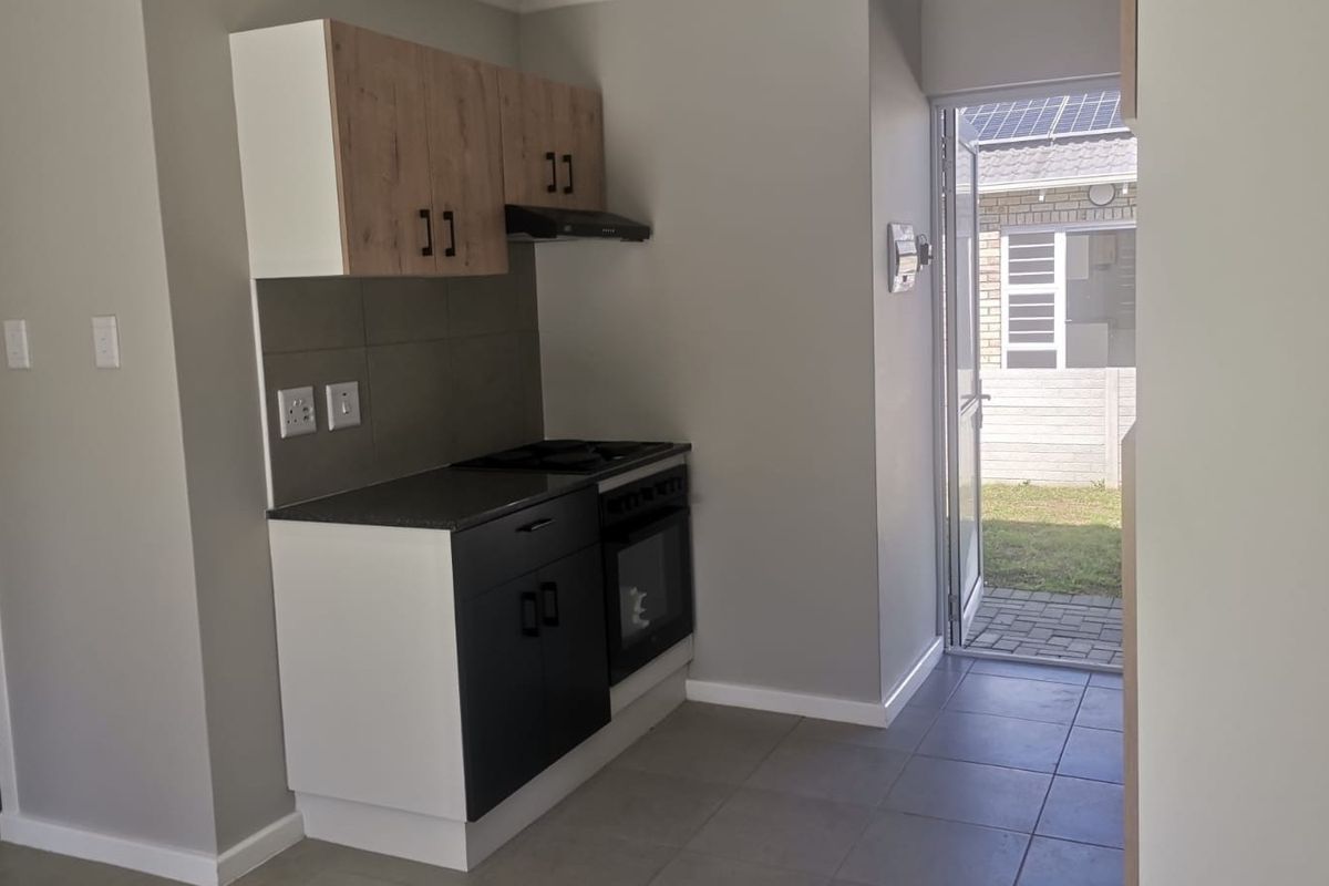 A compact, modern kitchen featuring built-in cabinetry, a hob, oven, and extractor fan, with direct access to the rear exterior area.