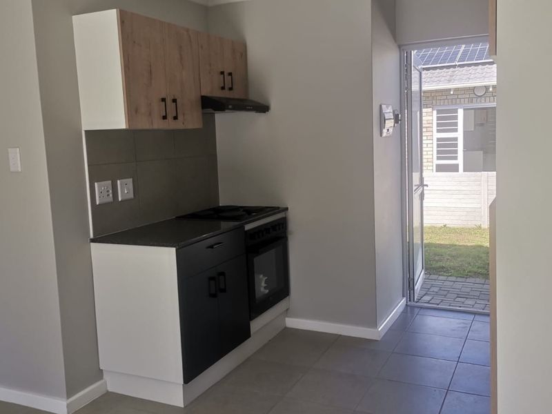 A compact, modern kitchen featuring built-in cabinetry, a hob, oven, and extractor fan, with direct access to the rear exterior area.