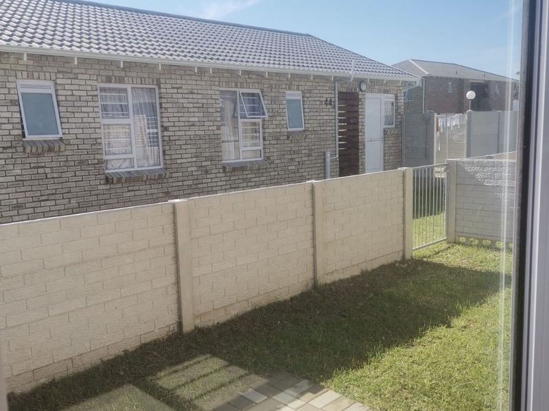 A view of the rear exterior of the townhouse, featuring a face brick facade, tiled roof, and a private garden with a precast boundary wall.