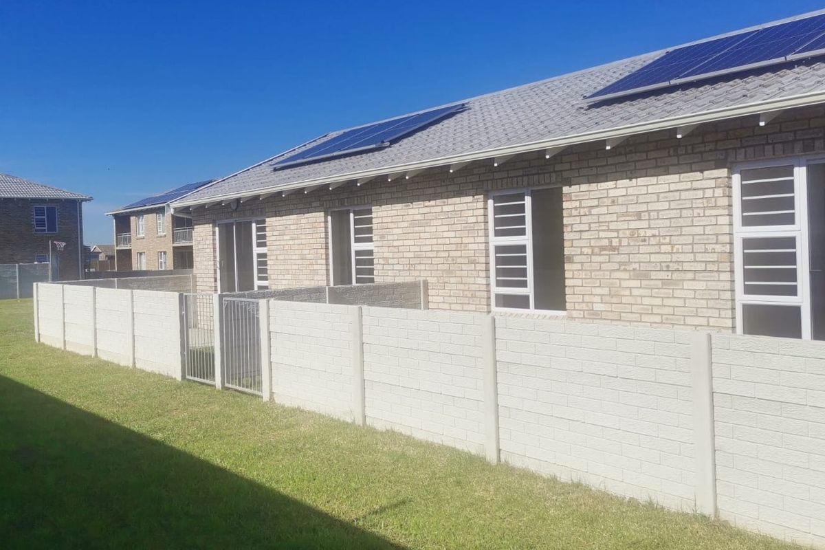 Rear view of the townhouse featuring a brick facade, solar panels on the roof, and a private enclosed garden area with a precast boundary wall.
