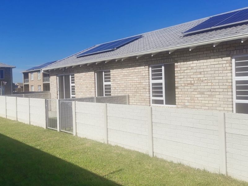Rear view of the townhouse featuring a brick facade, solar panels on the roof, and a private enclosed garden area with a precast boundary wall.