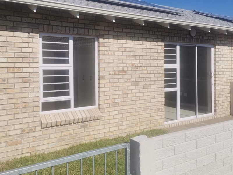 Rear exterior view of a face brick townhouse featuring sliding glass doors, security bars, and solar panels installed on the roof.