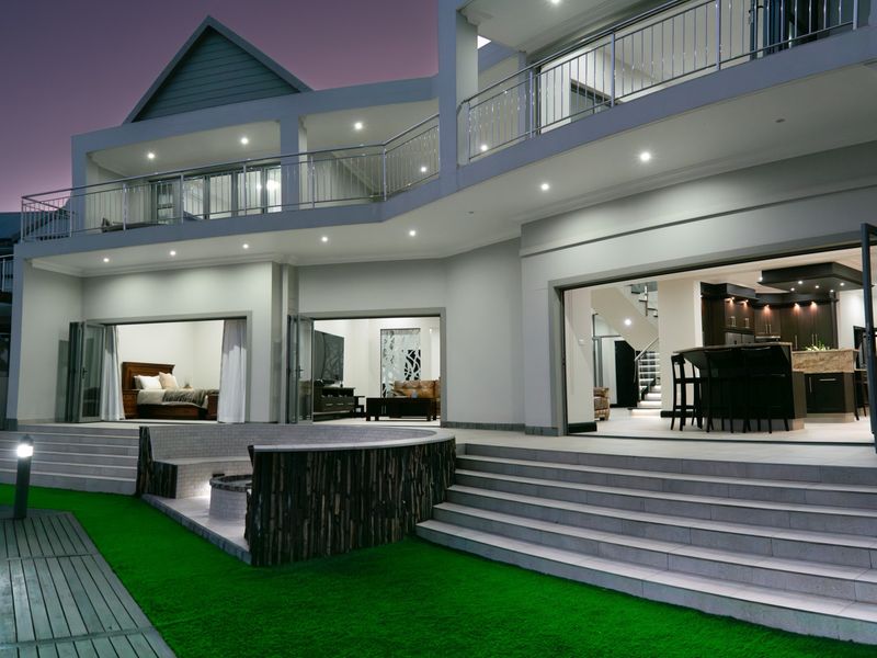 A modern double-story rear elevation featuring a spacious tiled patio, built-in fire pit, and seamless indoor-outdoor flow through large stacking glass doors.