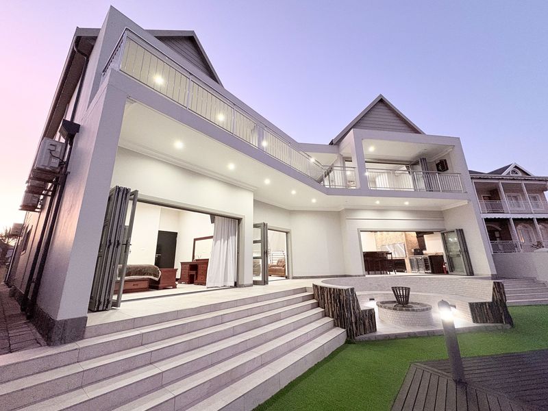 Modern rear elevation featuring expansive bi-fold doors, a spacious tiled patio with a sunken fire pit, and an upper-level balcony with metal railings.