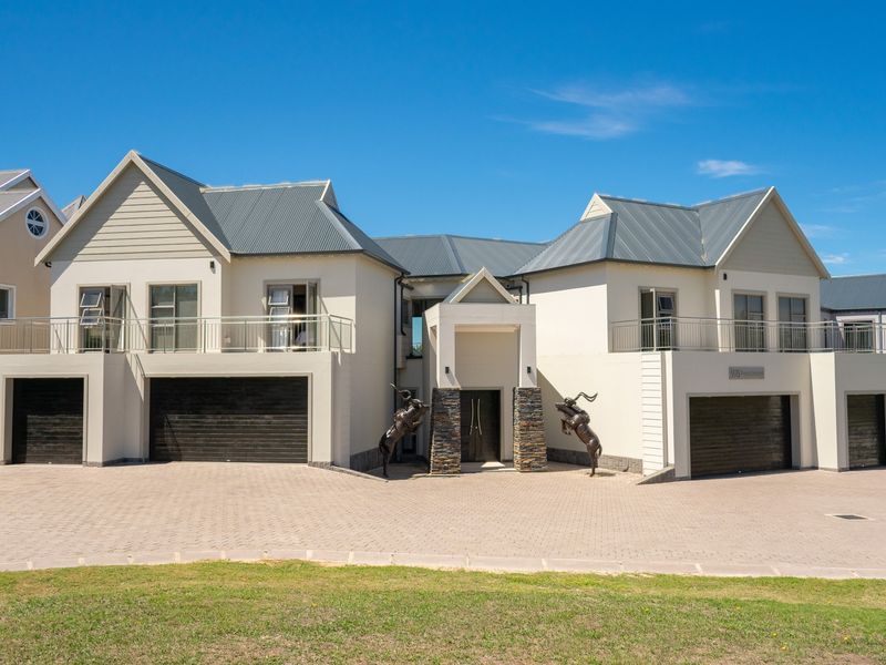 A modern double-story residence featuring a paved driveway, dual garages, stone-clad entrance pillars, and upper-level balconies with steel railings.
