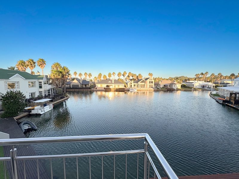 A scenic elevated view overlooking a tranquil canal with surrounding residential properties, featuring a modern stainless steel balustrade in the foreground.