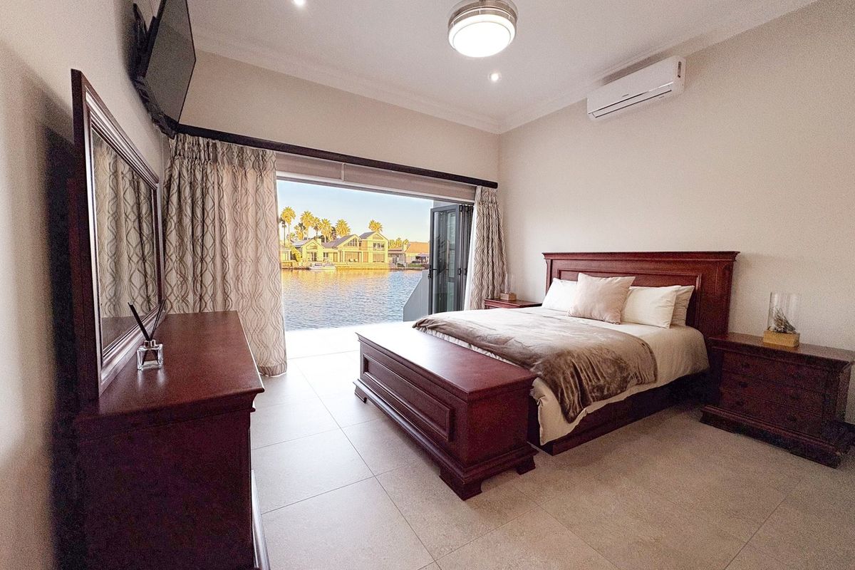 Spacious bedroom featuring tiled flooring, split-system air conditioning, and large stacking glass doors opening to a scenic waterfront view.