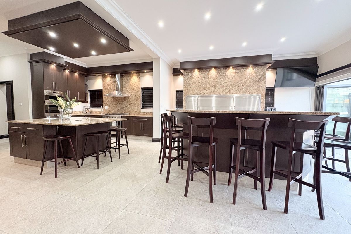 Spacious modern kitchen featuring dark wood cabinetry, granite countertops, a large central island, breakfast bar seating, and high-end built-in appliances.