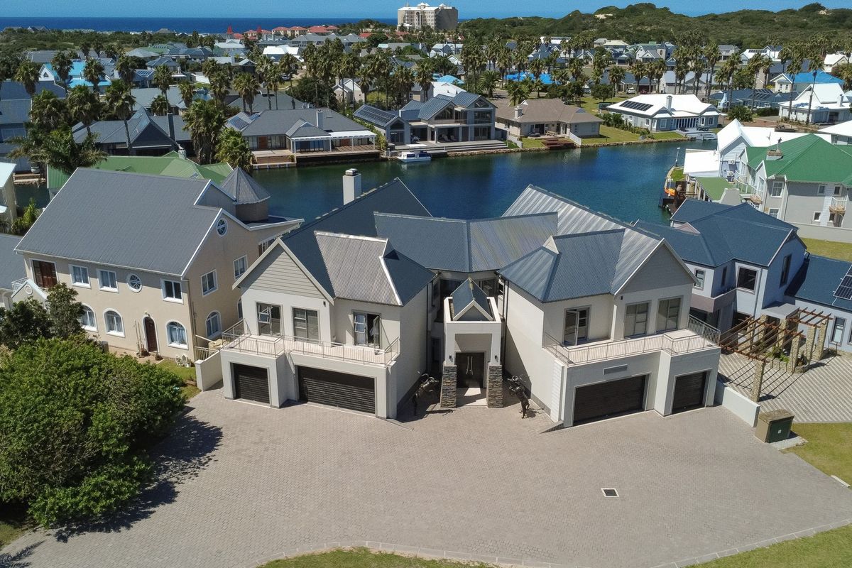 Aerial view of a modern waterfront residence featuring a paved driveway, multiple garages, and balconies overlooking the canal in a secure estate.