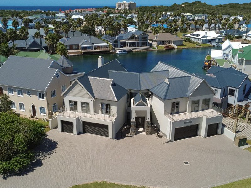Aerial view of a modern waterfront residence featuring a paved driveway, multiple garages, and balconies overlooking the canal in a secure estate.