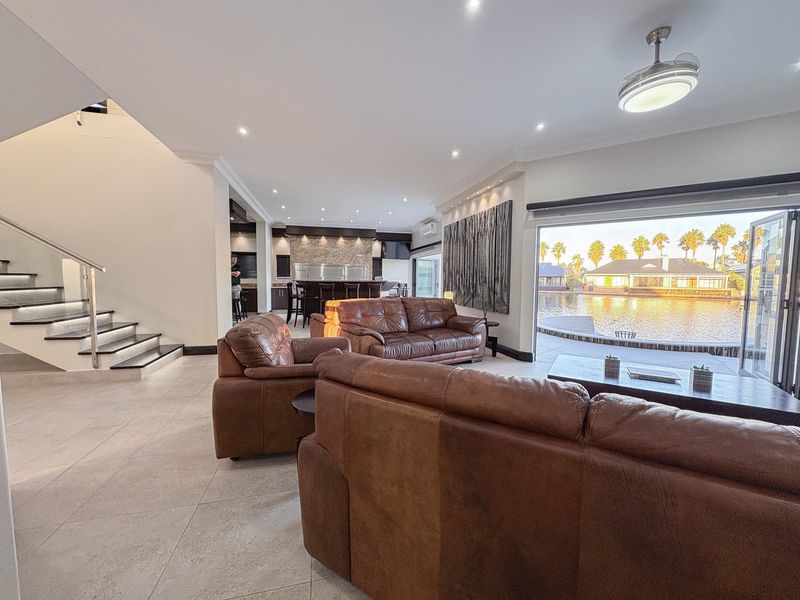 Spacious open-plan living area featuring modern tiled floors, a sleek staircase with glass balustrades, and seamless flow to a waterfront patio through stacking doors.