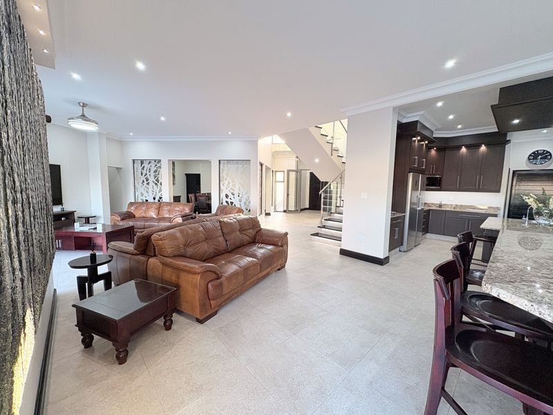 Spacious open-plan living area featuring a modern kitchen with dark cabinetry, granite countertops, and a sleek staircase with a glass balustrade.