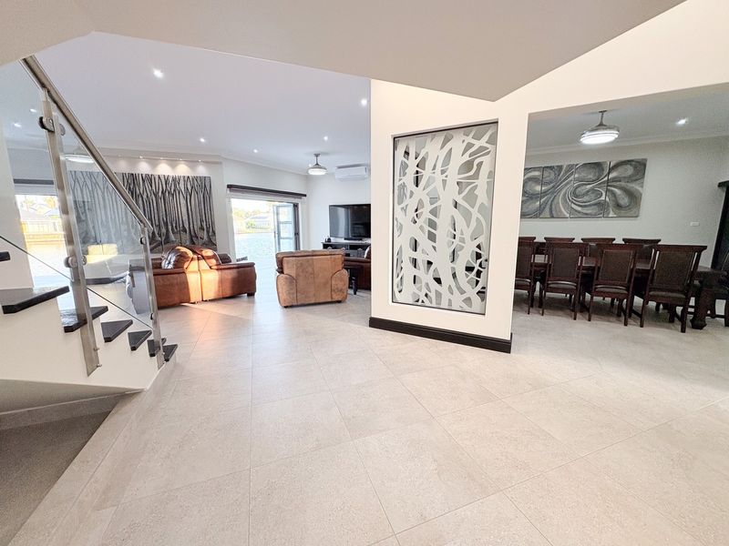 Spacious open-plan living and dining area featuring modern tiled flooring, a feature room divider, and a contemporary staircase with glass balustrades.