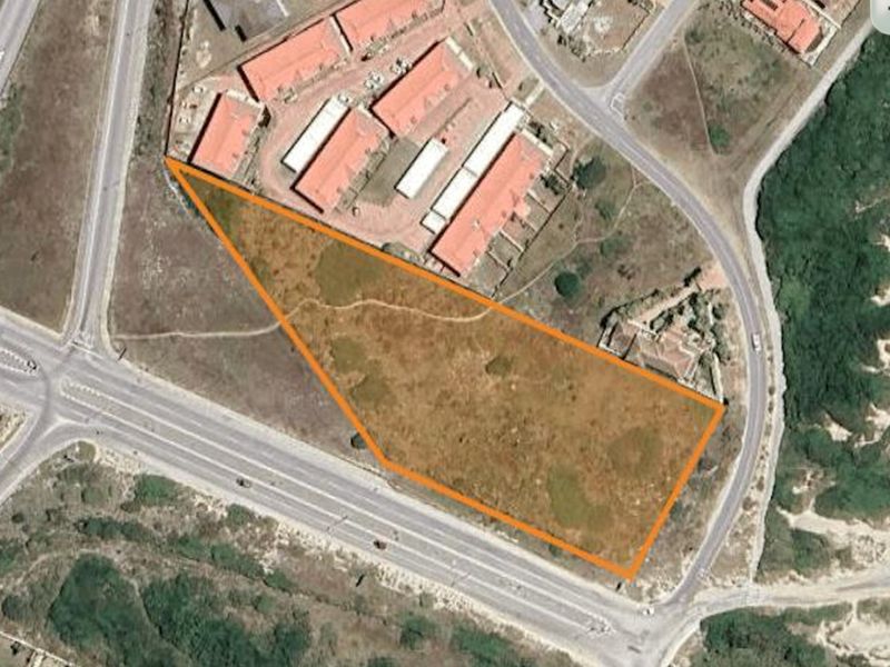An aerial view of a vacant residential plot of land with clear boundary markings, situated near existing residential developments and main road access.