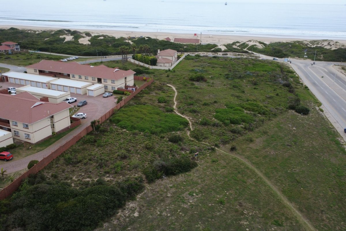 Aerial view of a vacant residential plot situated near the coastline, adjacent to an existing residential complex and main road.