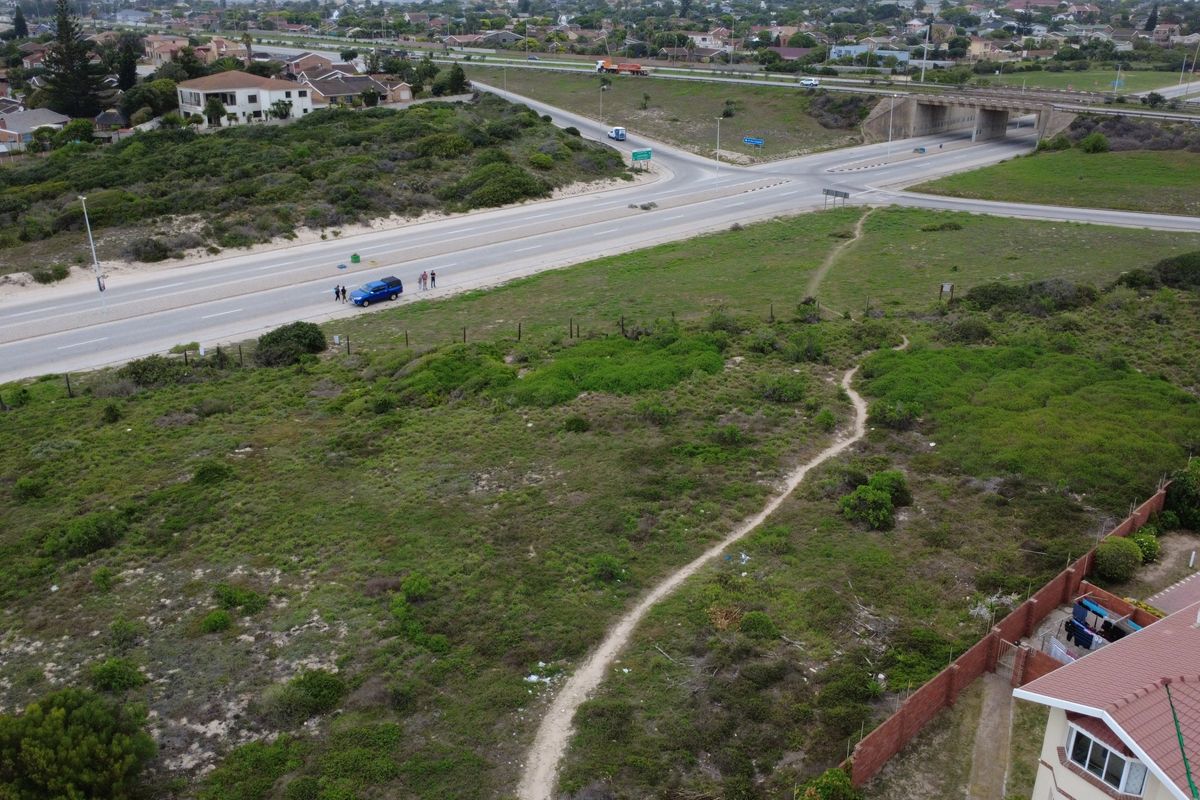 Aerial view of a vacant residential plot featuring natural vegetation, perimeter fencing, and an unpaved access path near a main road.