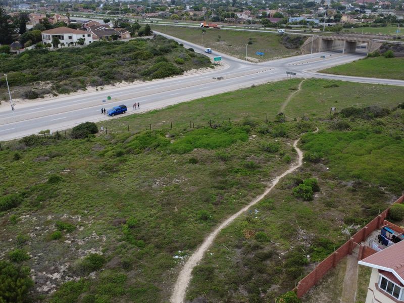 Aerial view of a vacant residential plot featuring natural vegetation, perimeter fencing, and an unpaved access path near a main road.