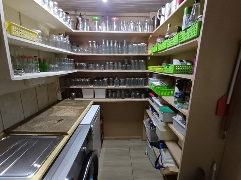 Functional scullery or pantry area featuring extensive built-in shelving, a stainless steel sink, and tiled splashback, providing ample storage and utility space.