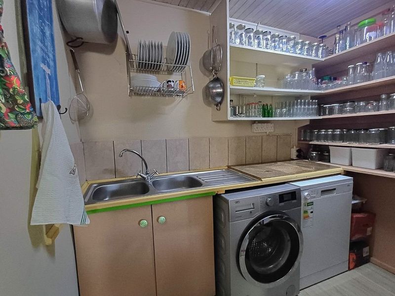 Functional scullery area featuring a double basin sink, tiled splashback, built-in cabinetry, and ample open shelving for storage.