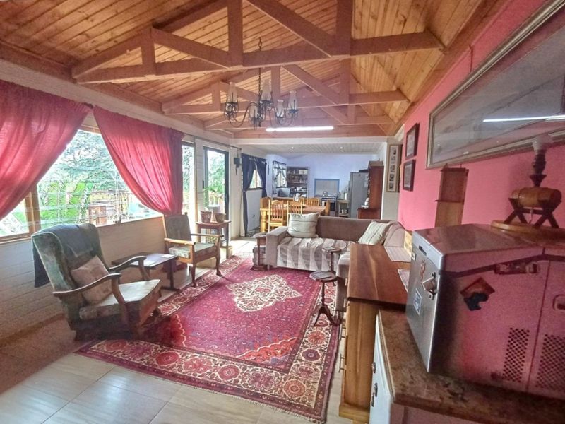 Spacious open-plan living area featuring a high exposed timber truss ceiling, tiled flooring, and large windows providing natural light.