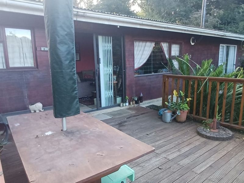 A wooden deck patio area featuring a timber balustrade and sliding door access to the interior, showing signs of weathering and wear.